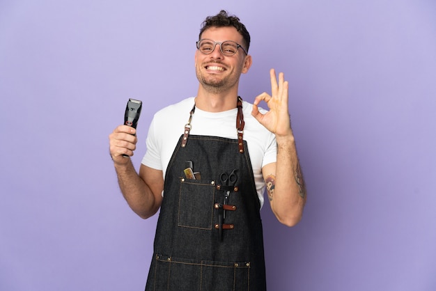 Barber caucasian man in an apron isolated on purple showing ok sign with fingers