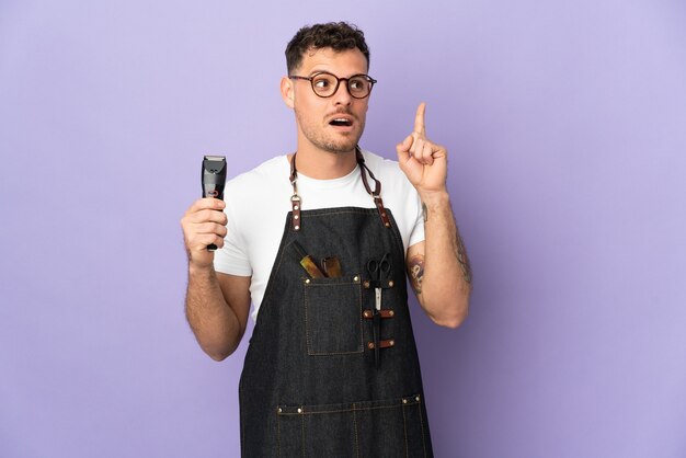 Barber caucasian man in an apron isolated on purple thinking an idea pointing the finger up