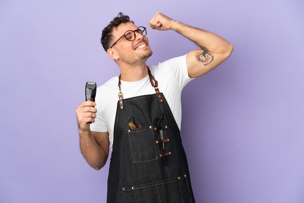 Barber caucasian man in an apron isolated on purple wall celebrating a victory