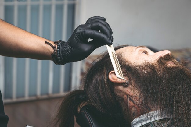 Barber combing red beard in barbershop.