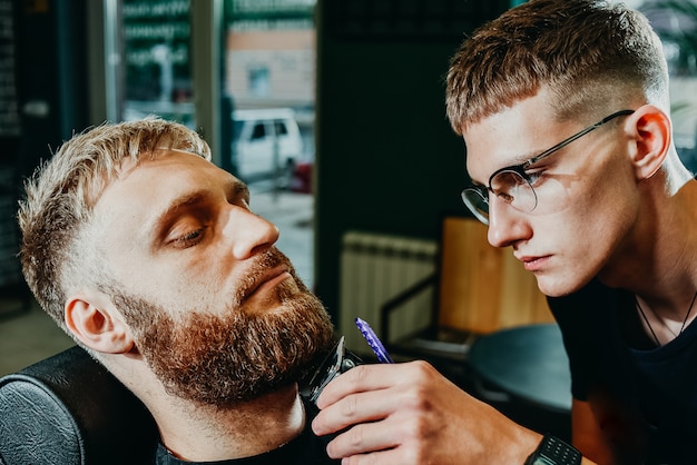 Photo the barber cuts his beard to a man in the salon