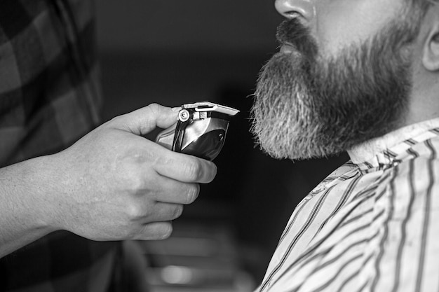 Парикмахер стрижет бороду бритвой и машинкой для стрижки