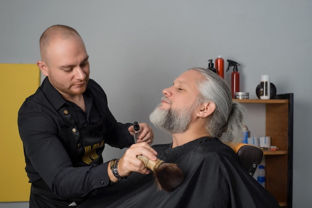 Barber cutting and styling the beard of a grayhaired man B Barber shop for men