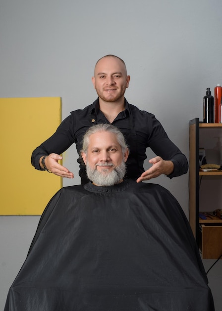 Barber cutting and styling the beard of a grayhaired man Barber shop for men