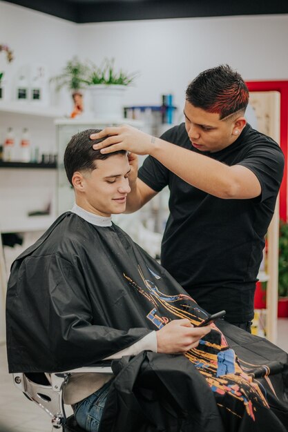 Foto barbiere che rifinisce il taglio di capelli con la lama mentre il cliente controlla il cellulare