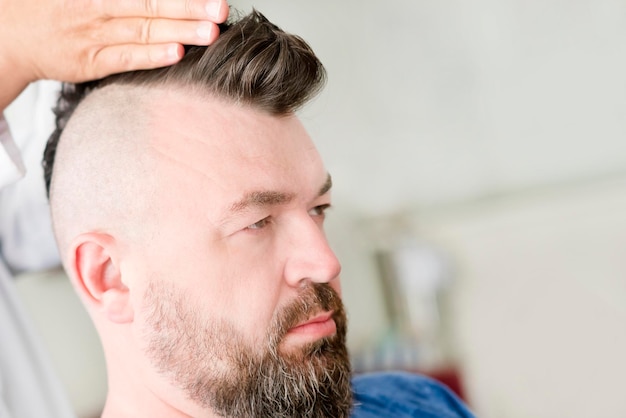 Barber maakt een mohawk-kapsel van een volwassen man met baard