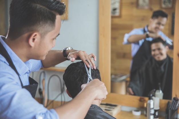 Barbiere che fa taglio di capelli dell'uomo attraente nel negozio di barbiere