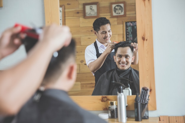 Barber making haircut of attractive man in barbershop