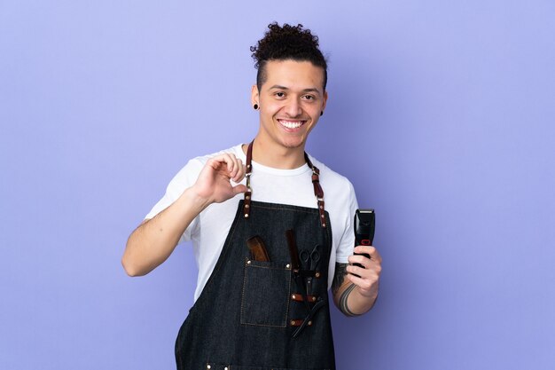 Barber man in an apron over isolated purple wall proud and self-satisfied