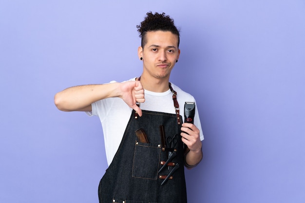 Photo barber man in an apron over isolated purple wall showing thumb down sign