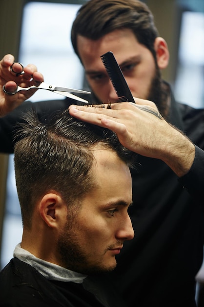 The Barber a man with a beard in the process of cutting the client a pair of scissors in the Barbershop