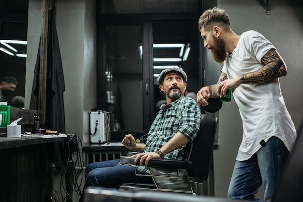 парикмахер, опираясь одной рукой на кресло, наклоняется к клиенту