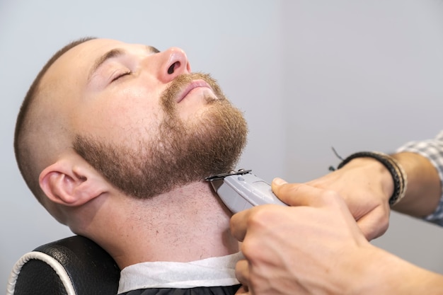 barber shaves his client's beard with an electric trimmer.