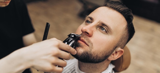 Barbiere tosatura della barba all'uomo nel negozio di barbiere che incornicia l'attaccatura dei capelli rasoio elettrico vintage tinto di marrone