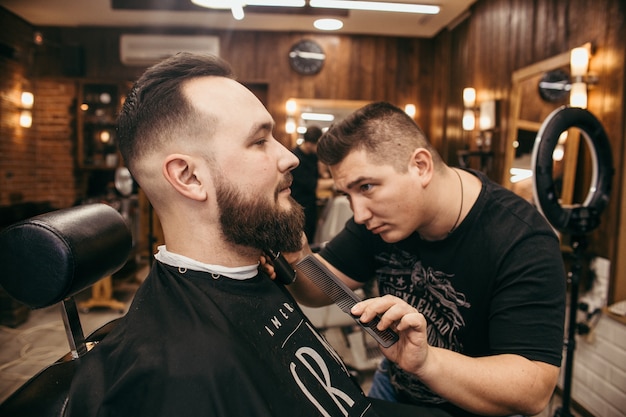 Barber shop, a man with a beard cut hairdresser. Professional haircut, retro hairstyle and styling. Beautiful hair and care, hair salon for men. Customer service.