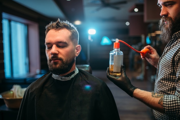 Barber splashing client face by aftershave lotion