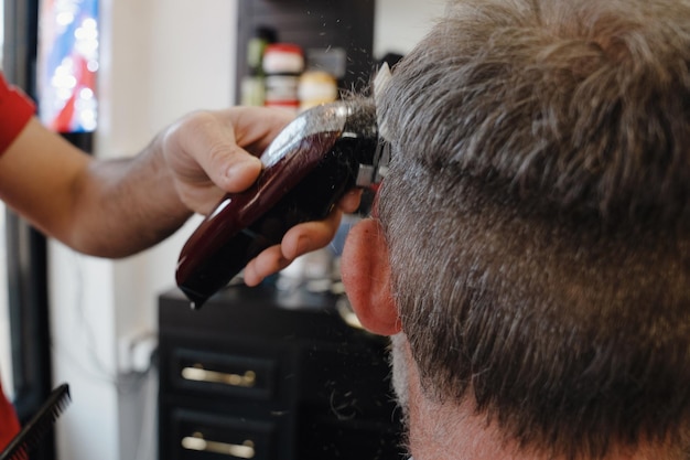 Barber trimming and cutting bearded man with shaving machine in barbershop Hairstyling process