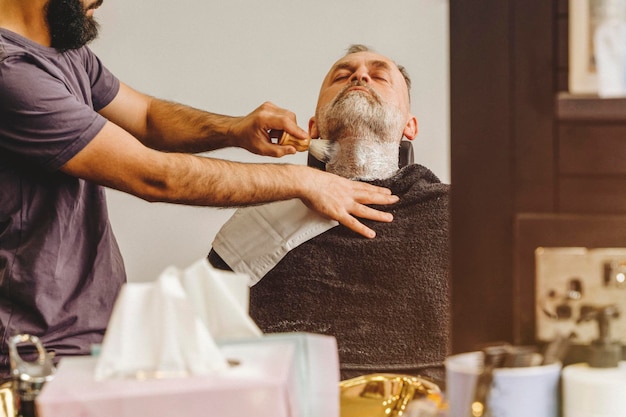 Barber trimming and cutting bearded man with shaving machine in barbershop Hairstyling process