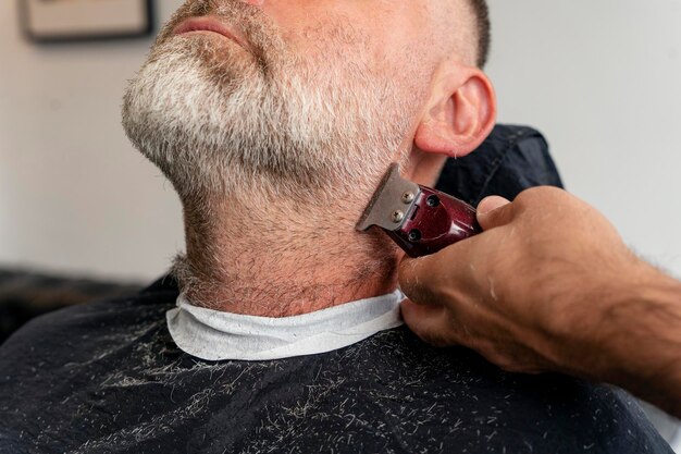 Barber trimming and cutting bearded man with shaving machine in barbershop Hairstyling process