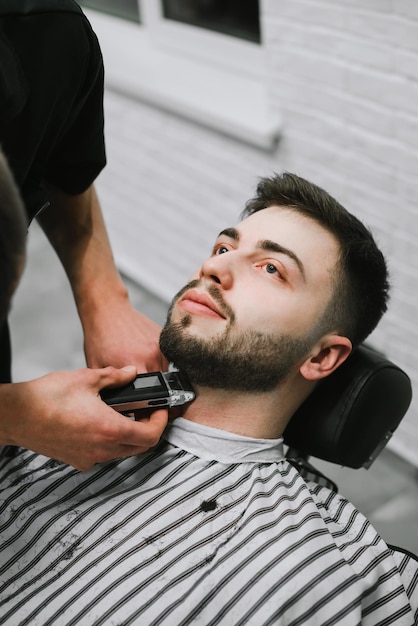 Barber trims his beard seriously to the client Vertical closeup portrait