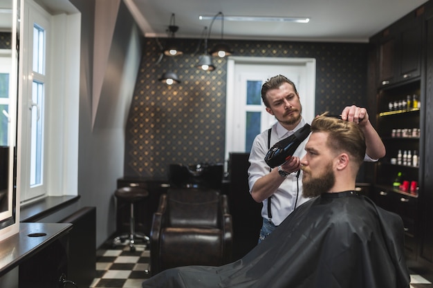 Barbiere con asciugatrice per asciugare i capelli dell'uomo