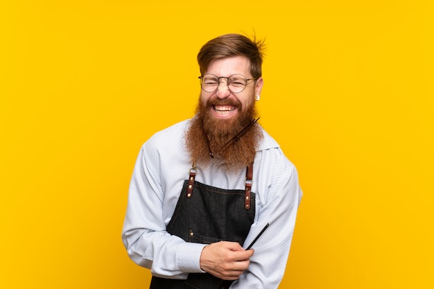 Barber with long beard in an apron over isolated yellow background