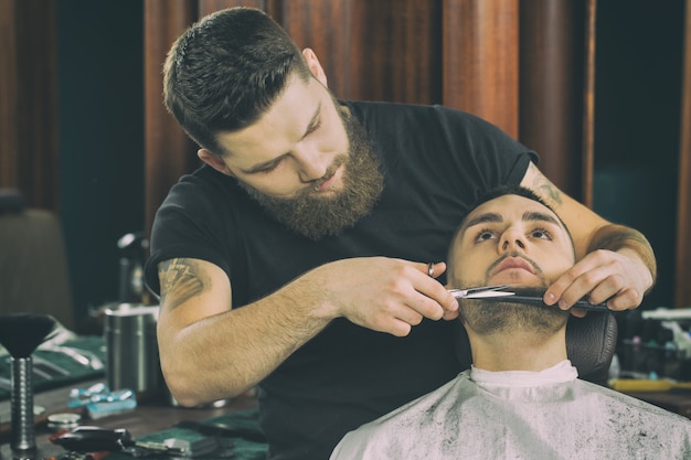Barber at work. Horizontal portrait of a handsome bearded and tattooed barber working