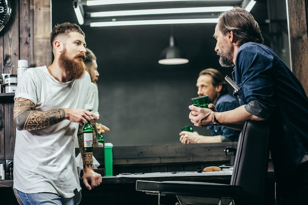 barbers standing in front of each other and talking while drinking beer