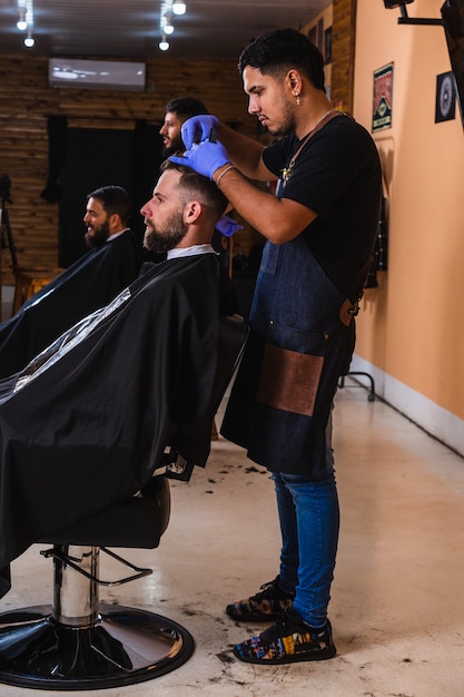 Barbers working in their men's salon - Two bearded barbers giving haircuts to male customers in the barber shop .