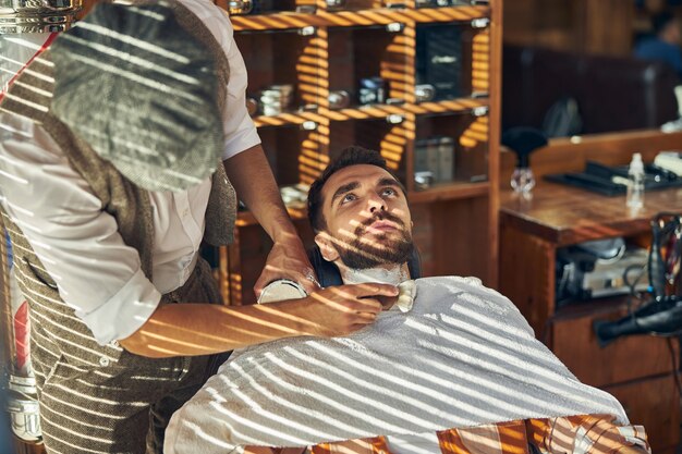 シェービング手順の前に肘掛け椅子にもたれかかっている理髪店の顧客
