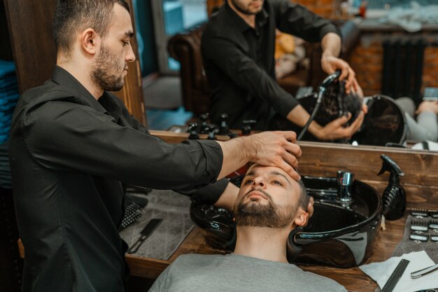 Barbiere, un uomo si lava i capelli. barber lava il suo cliente. lavare i capelli e le barbe dopo il taglio. cura personale