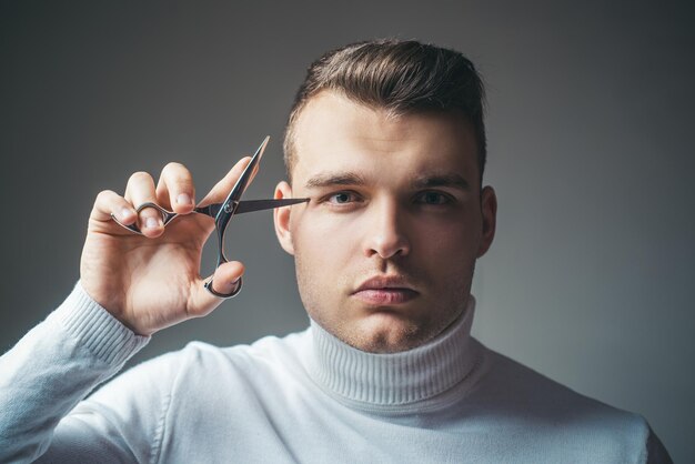 Foto concetto di servizio di parrucchiere. attrezzatura professionale da barbiere. taglio di capelli. forbici da presa per il viso rigoroso dell'uomo. l'acconciatura lucida del barbiere tiene le forbici d'acciaio. crea il tuo stile. capelli tagliati dal barbiere sicuro di sé macho