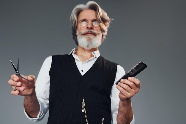 Foto strumenti da barbiere su sfondo grigio l'uomo anziano moderno ed elegante con i capelli grigi e la barba è al chiuso
