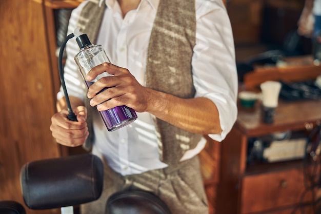 Photo a barbershop worker holding a spray bottle with a purple liquid inside