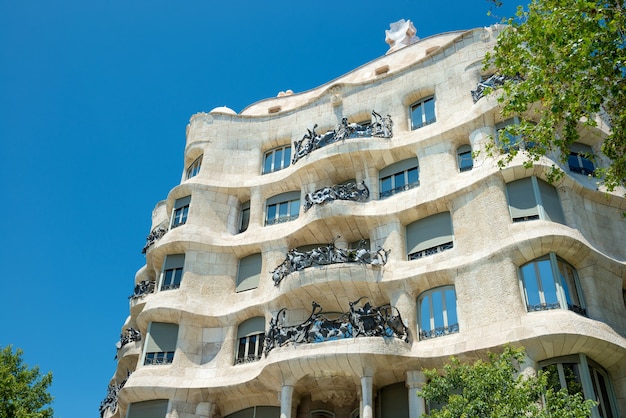 바르셀로나, 스페인 - 2016년 5월 21일: 스페인 바르셀로나 거리에 푸른 나무가 있는 카사 밀라의 외관. 유네스코 목록에 포함된 안토니 가우디가 설계한 유명한 건물