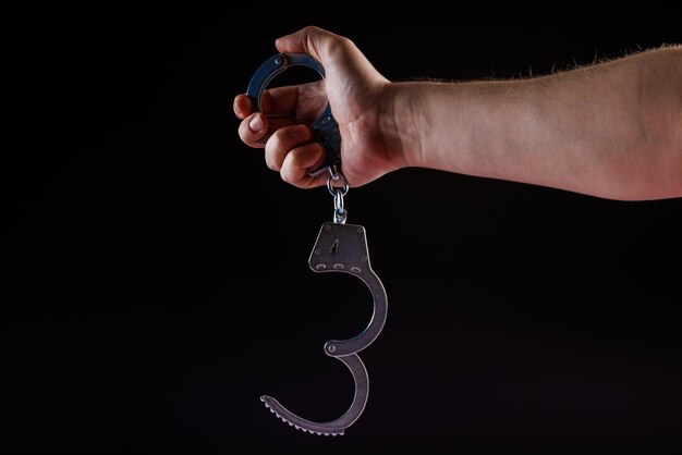Голая кавказская рука, держащая открытые серебряные стальные наручники на черном фоне.