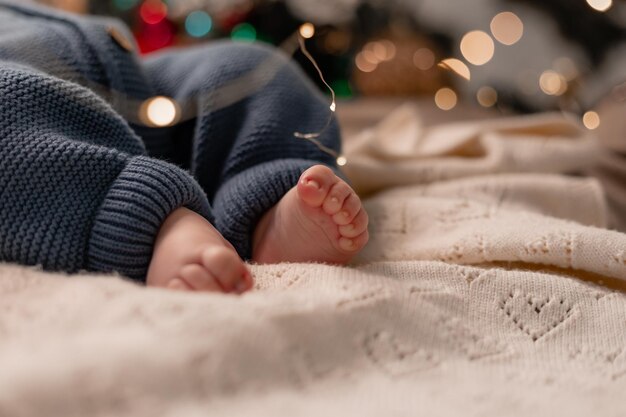 Piedi nudi di un bambino in una tuta blu in maglia sdraiata su una coperta leggera sul pavimento sotto il primo piano dell'albero di natale. vacanze invernali, momenti divertenti, natale bambino. foto di alta qualità