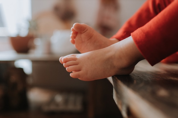 bare feet of a child in red trousers sitting on a wooden chair space for text