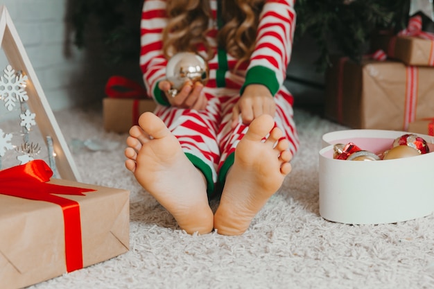 Photo bare feet of a child sitting on the floor near the christmas tree. close-up.winter new year concept. christmas