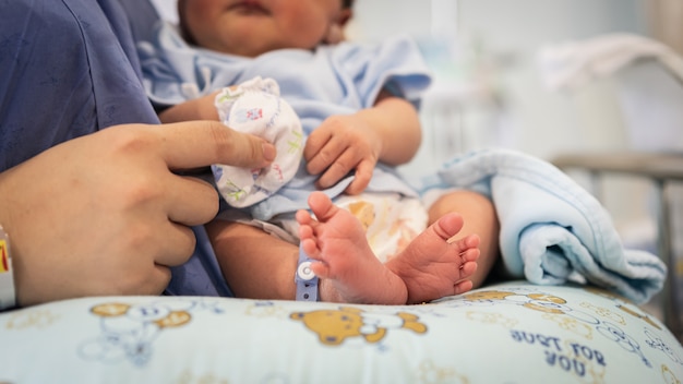 Bare feet of a cute newborn baby in a tender embrace of mother.