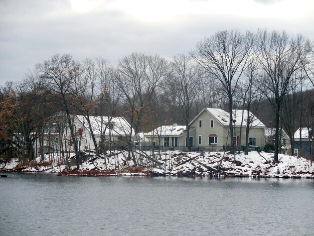 Bare trees by lake and buildings against sky during winter