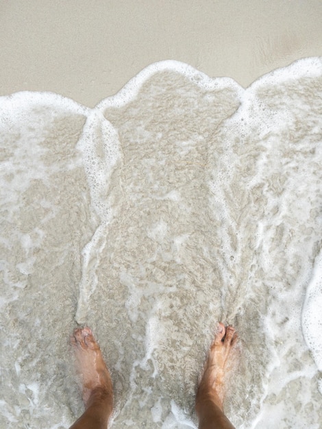 I piedi nudi sulla spiaggia con la schiuma bianca dell'onda