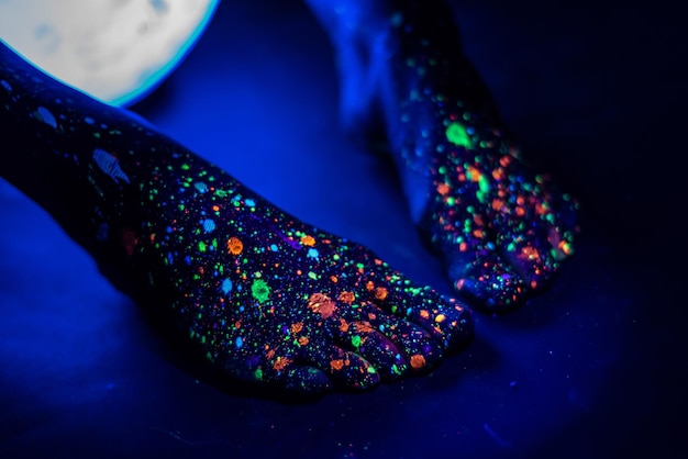 Barefoot female feet in a spray of paint glowing in the dark Toes in fluorescent powder Body art glowing in ultraviolet light like a blue night sky with stars Close up