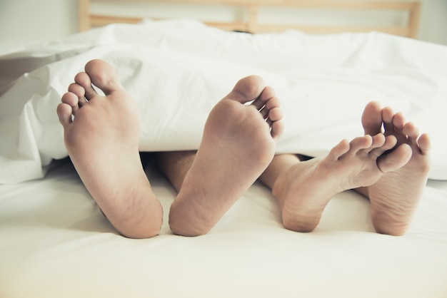 Barefoot of lovers under blanket in bedroom