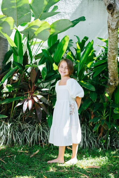 Barefoot meisje in een witte jurk staat in een tropische tuin