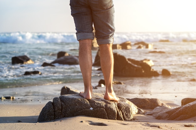 Босоногий человек, стоящий на пляже на закате с видом на ноги