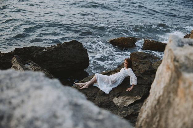 Barefoot woman lying on rocky coast with cracks on rocky\
surface view from above