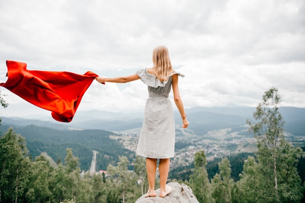 Barefoot woman stands at stone, waving red blanket