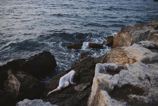 Barefoot woman in a white dress lying on a stone in a white dress landscape