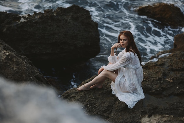 Barefoot woman in white dress sits on a cliff nature top view High quality photo